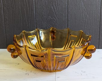 May include: Amber glass bowl with a fluted design and two small knobs on each side. The bowl has a geometric pattern.