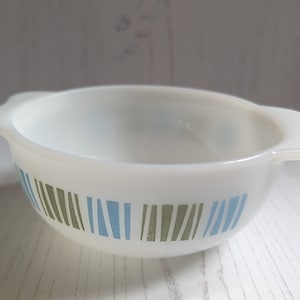 May include: White ceramic bowl with blue and green striped pattern. The bowl has two handles on the sides.