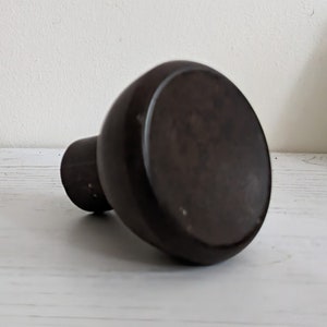 May include: A dark brown ceramic vase with a rounded bottom and a wide opening. The vase is sitting on a white surface.