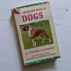 May include: A vintage book titled "The Observer's Book of Dogs" by Clifford L.B. Hubbard. The cover features a brown and white Boxer dog standing on a green grassy field. The book has 148 illustrations and describes 300 breeds and varieties of dogs.
