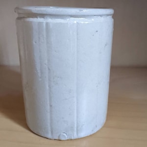 Può includere: Un vaso di ceramica bianca con nervature verticali. Il vaso ha una superficie liscia e leggermente ruvida.