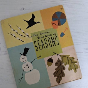 Może przedstawiać: Antyczna książka dla dzieci zatytułowana "The Junior True Book of Seasons". Okładka przedstawia ilustracje ptaka, bałwana, żołędzia i piłki plażowej.