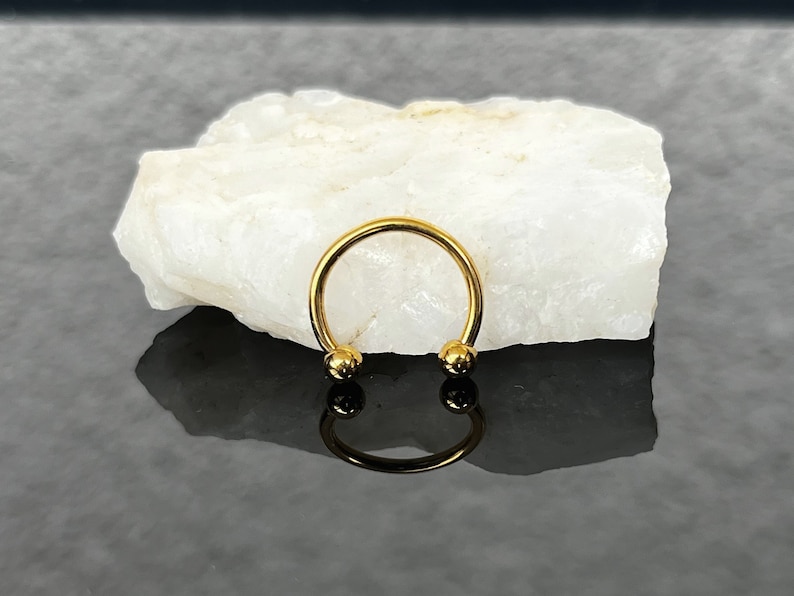 May include: Gold horseshoe shaped ring with two round balls on the ends.