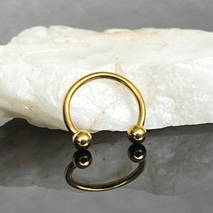 May include: Gold circular barbell with two round balls on the ends. The barbell is on a white rock surface.