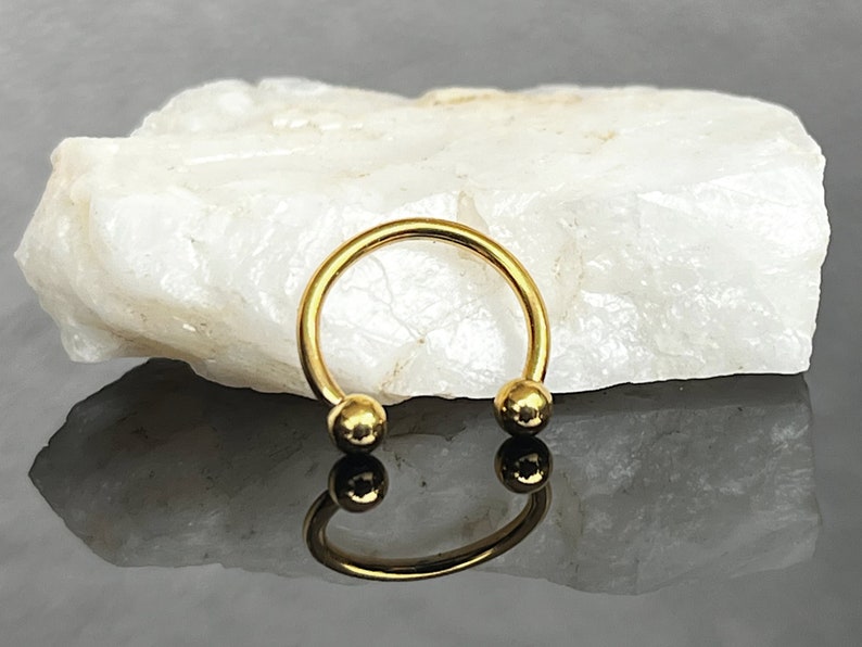 May include: Gold circular barbell with two round balls on the ends. The barbell is on a white rock surface.