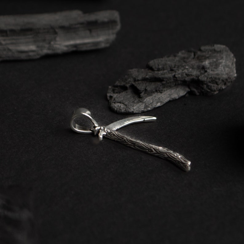 May include: A silver pendant in the shape of a stylized tree branch with a textured surface. The pendant is on a black background.