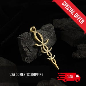May include: Gold pendant necklace featuring a detailed, intricate design of a stylized sword with a pointed tip. The pendant is displayed on a black background.