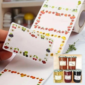 Op de afbeelding: Rol witte etiketten met kleurrijke fruit- en bloemenranden. De etiketten zijn rechthoekig met lege ruimtes om op te schrijven. De afbeelding toont ook verschillende potten jam met etiketten.