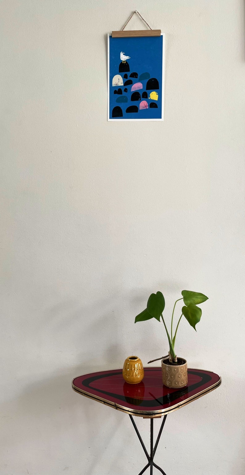 May include: A red and black tri-legged table with a rounded, asymmetrical top. A yellow ceramic vase and a potted plant with green leaves are on the table.