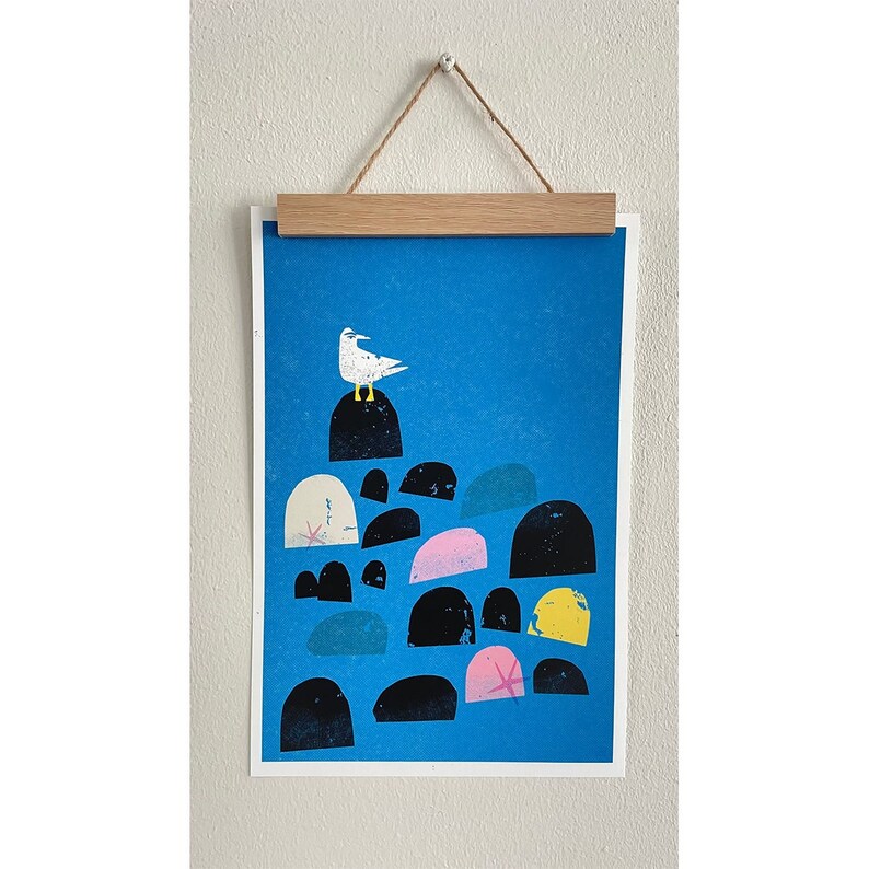 May include: A blue and white print of a seagull perched on a stack of rocks. The rocks are various shades of gray, black, pink, and yellow.