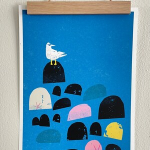 May include: A blue and white print of a seagull perched on a rock with a starfish in the foreground. The print features a variety of black, white, pink, and yellow rocks.