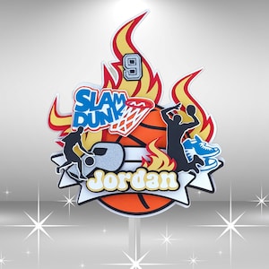 May include: A basketball cake topper with a basketball, flames, a basketball player, and the words "Slam Dunk" and "Jordan".