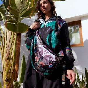 Puede incluir: Chaqueta negra con un llamativo diseño de alas de pájaro en tonos verdes, morados y naranjas. Se complementa con un bolso bandolera a juego. El diseño es audaz y moderno.