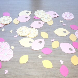 Puede incluir: Una colecci&oacute;n de recortes de papel con forma de limones y corazones. Los limones son de color amarillo y rosa, y los corazones son rosas. Los recortes est&aacute;n dispuestos sobre una superficie marr&oacute;n claro.