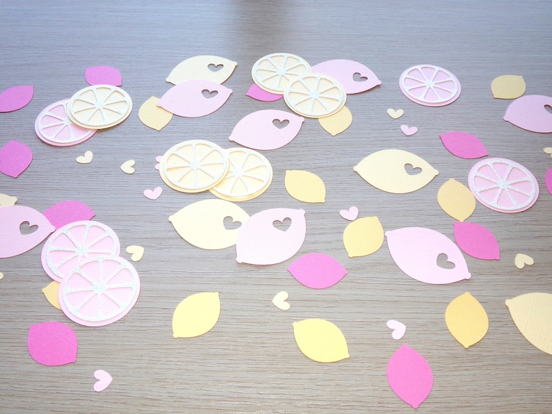 Puede incluir: Una colecci&oacute;n de recortes de papel con forma de limones y corazones. Los limones son de color amarillo y rosa, y los corazones son rosas. Los recortes est&aacute;n dispuestos sobre una superficie marr&oacute;n claro.