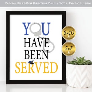 Può includere: Stampa incorniciata con le parole "YOU HAVE BEEN SERVED" in blu, nero e giallo. L'immagine include manette e una grafica di cappello della polizia. Due adesivi circolari indicano le dimensioni 20x25 cm e 13x18 cm. Una pianta succulenta in un vaso bianco è in primo piano.
