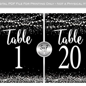 May include: Set of 20 black and silver table number cards with a silver glitter background and white string lights. The cards are 5x7 inches and feature the text "Table" followed by the table number.