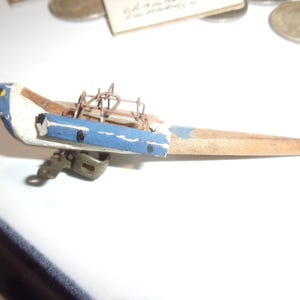 May include: A vintage wooden bird-shaped toy with a blue and white painted head and a long, pointed wooden body. It features a metal mechanism and is likely a pull-along or wind-up toy. The toy is set against a white background.