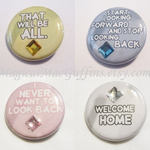 May include: Four 1-inch button pins with different sayings and rhinestones. The first pin is yellow with the text "THAT WILL BE ALL." The second pin is blue with the text "START LOOKING FORWARD AND STOP LOOKING BACK." The third pin is pink with the text "I NEVER WANT TO LOOK BACK." The fourth pin is white with the text "WELCOME HOME."