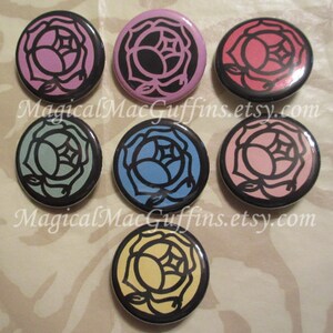 May include: Set of eight 1-inch button badges featuring a black outline of a rose with different coloured centres. The colours include pink, light blue, yellow, light green, red, light pink, purple, and dark blue.