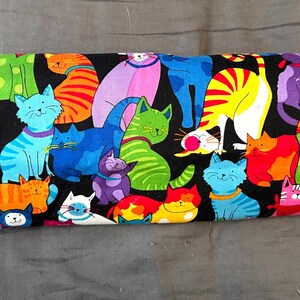 May include: A colorful cat-themed fabric with a black background. The fabric features various cartoon cats in shades of blue, green, orange, pink, and purple. Some cats wear bandanas or collars. The design is playful and suitable for various craft projects.