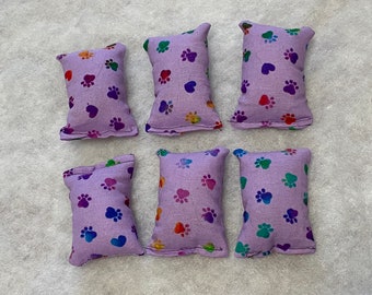 May include: Six rectangular lavender fabric pouches arranged in two rows. Each pouch features a repeating pattern of small, multicolored paw prints and hearts in shades of red, orange, yellow, green, blue, and purple across the surface.