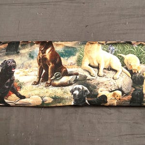May include: A decorative fabric strip featuring a variety of Labrador Retrievers in different colors, including black, brown, and yellow. The dogs are depicted in various poses, some with puppies, in a natural outdoor setting.