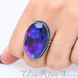 Op de afbeelding: Een zilveren ring met een grote ovale edelsteen. De edelsteen is donkerpaars en blauw van kleur met een galaxy-achtig patroon.