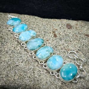 May include: A silver bracelet with a chain link design and seven oval-shaped blue and white gemstone beads.