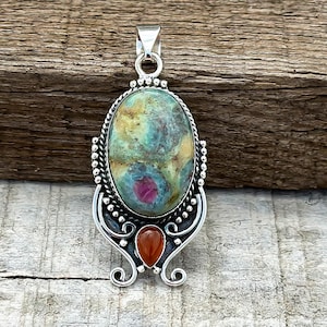 May include: A silver pendant with a large oval green, pink, and yellow gemstone set in a silver filigree design. A smaller orange gemstone is set below the larger stone.