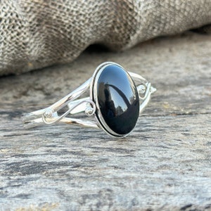Könnte beinhalten: Ein silbernes Armband mit einem schwarzen ovalen Edelstein. Das Armband hat ein zartes, verziertes Design.