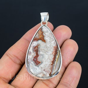 Puede incluir: Un colgante en forma de lágrima con un engaste de plata y una piedra de ágata marrón, blanca y roja.