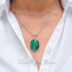 Pode incluir: Um colar de corrente de prata com um pingente oval verde. O pingente é engastado em prata e tem um acabamento liso e polido.