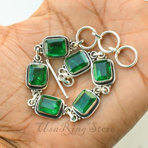 Op de afbeelding: Een zilveren armband met vijf smaragdgeslepen groene edelstenen in gepolijste metalen zettingen. De armband heeft een knevelsluiting met een staafje en drie ronde ringen voor verstelling. De tekst UsaRing Store is onderaan zichtbaar.