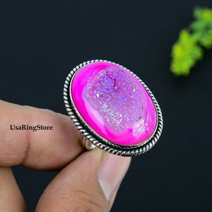 May include: A silver ring with a large oval pink and white agate gemstone. The ring has a detailed silver band.