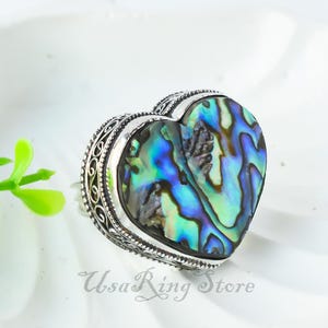 May include: A silver heart-shaped ring with an abalone shell inlay. The shell has a blue, green, and purple iridescent pattern.