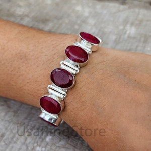 Könnte beinhalten: Ein silbernes Armband mit sechs ovalen roten Edelsteinen. Das Armband befindet sich an einem Handgelenk.