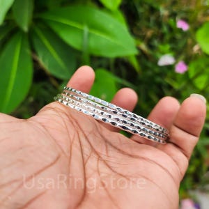 May include: Set of four silver bangles with a textured hammered finish. The bangles are stacked on top of each other.