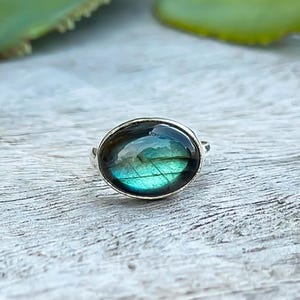 May include: A silver ring featuring a round, iridescent green and black gemstone.