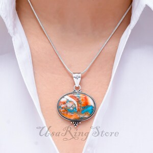 May include: A silver chain necklace with a pendant featuring a large oval-shaped turquoise stone with orange and white swirls. The stone is set in a silver bezel.
