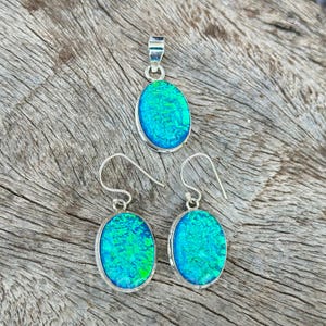 Op de afbeelding: Een set zilveren oorbellen en een hanger met ovale blauwe en groene opaalstenen.