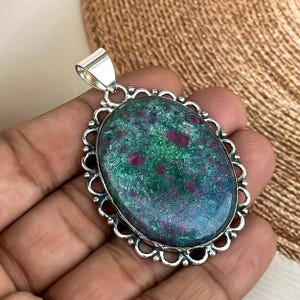 May include: Oval green and red gemstone pendant with a silver filigree frame. The pendant is set in a silver bail.