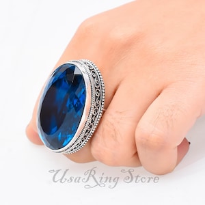 May include: A large, oval-shaped, blue gemstone ring with a silver band featuring intricate scrollwork.