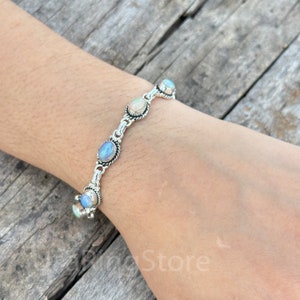 May include: A silver bracelet featuring five oval-shaped opal stones. The stones display a mix of blue, white, and iridescent hues.