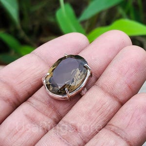 Puede incluir: Un anillo de plata con una gran piedra de cuarzo ahumado de forma ovalada. El anillo tiene un diseño simple y elegante.