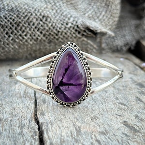 Peut inclure: Un bracelet en argent avec une pierre précieuse améthyste en forme de larme sertie dans une bélière perlée. Le bracelet a un design à double bande.