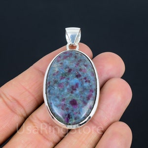May include: Oval shaped pendant with a blue and pink gemstone set in a silver frame.