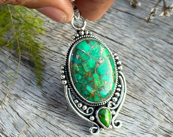 May include: A silver pendant with a large oval green turquoise stone and a smaller teardrop-shaped green turquoise stone. The pendant has intricate silver detailing.