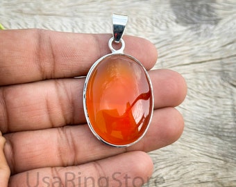 May include: An oval-shaped pendant featuring a smooth, translucent orange carnelian gemstone set in a polished silver frame with a silver bail at the top. The text UsaRingStore is visible in the lower portion of the image overlaying the skin.