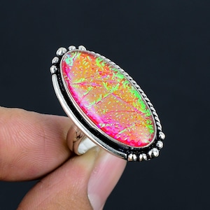 Peut inclure: Une bague en argent avec une pierre ovale en opale rose et verte. La bague a un bord perlé.